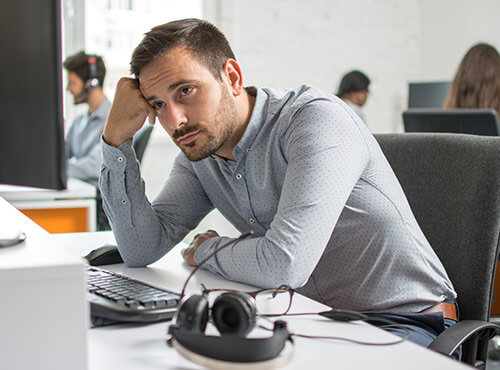 Lawaai en een slechte akoestiek op kantoor en in het callcenter Een man zit gestrest en vermoeid op zijn werkplek in het kantoor zonder geluidswering.
