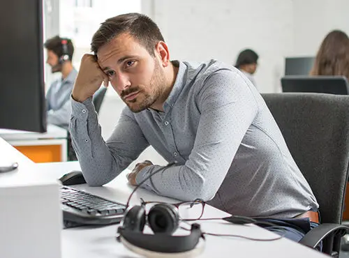Een man zit gestrest en vermoeid op zijn werkplek in het kantoor zonder geluidswering.