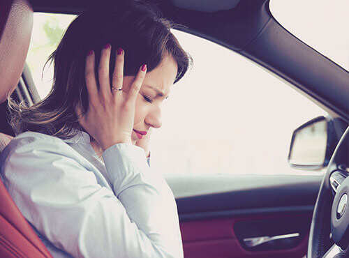 Lawaai in de wagen Een vrouw probeert zich te beschermen tegen het lawaai in de auto.