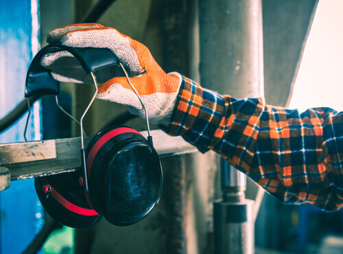 Gehoorbescherming en bescherming tegen geluidsoverlast in die industrie Een productiemedewerker pakt zijn gehoorbescherming erbij om zich te beschermen tegen een luidruchtige machine.