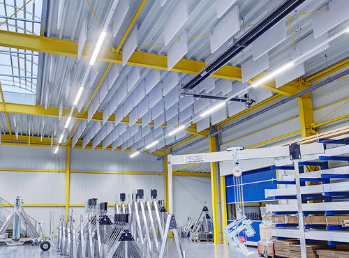 Akoestisch plafond als geluidsisolatie in een industriehal. Absorptieplaten hangend aan het plafond in een industriehal verminderen het lawaai.